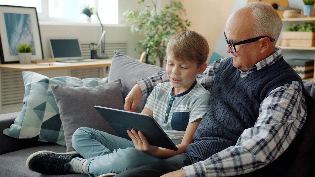 A grandfather and grandson looking at a tablet together on a sofa