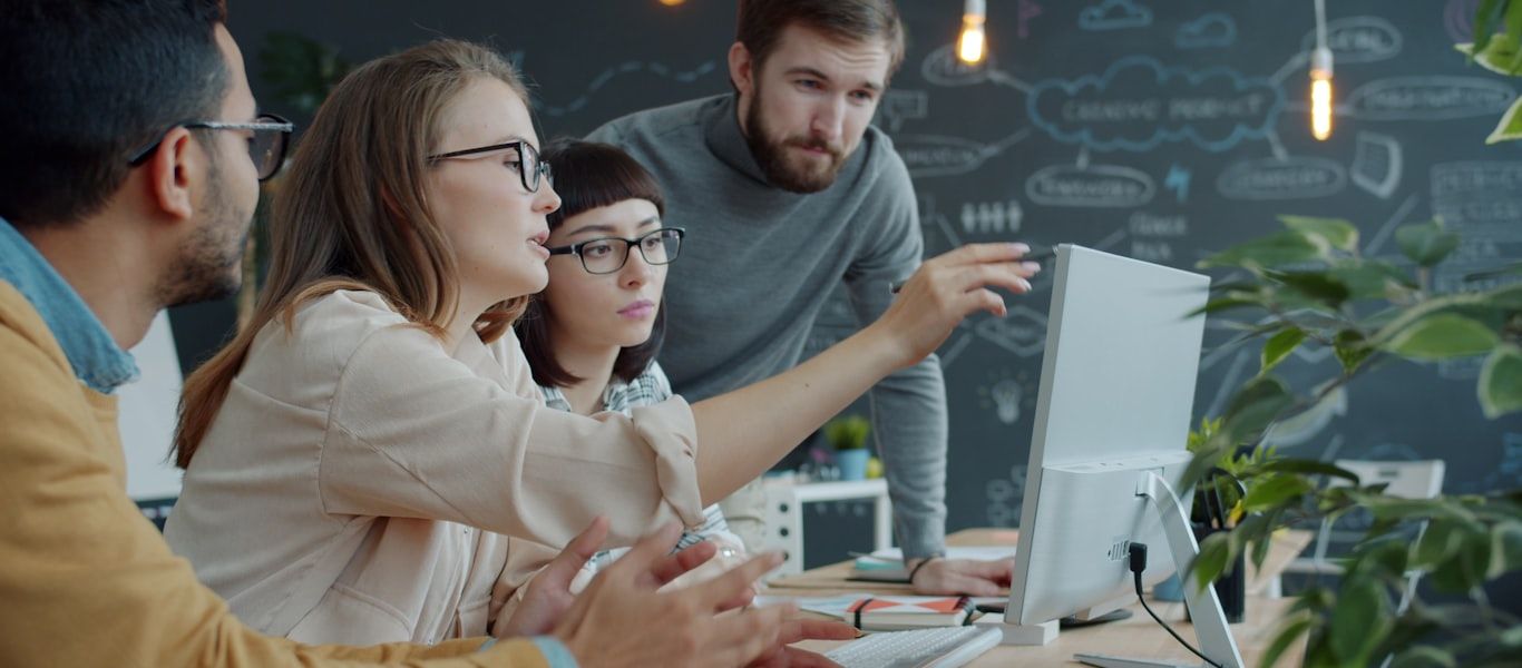 A team gathered around a monitor comparing options, an architecture diagram on the wall behind them
