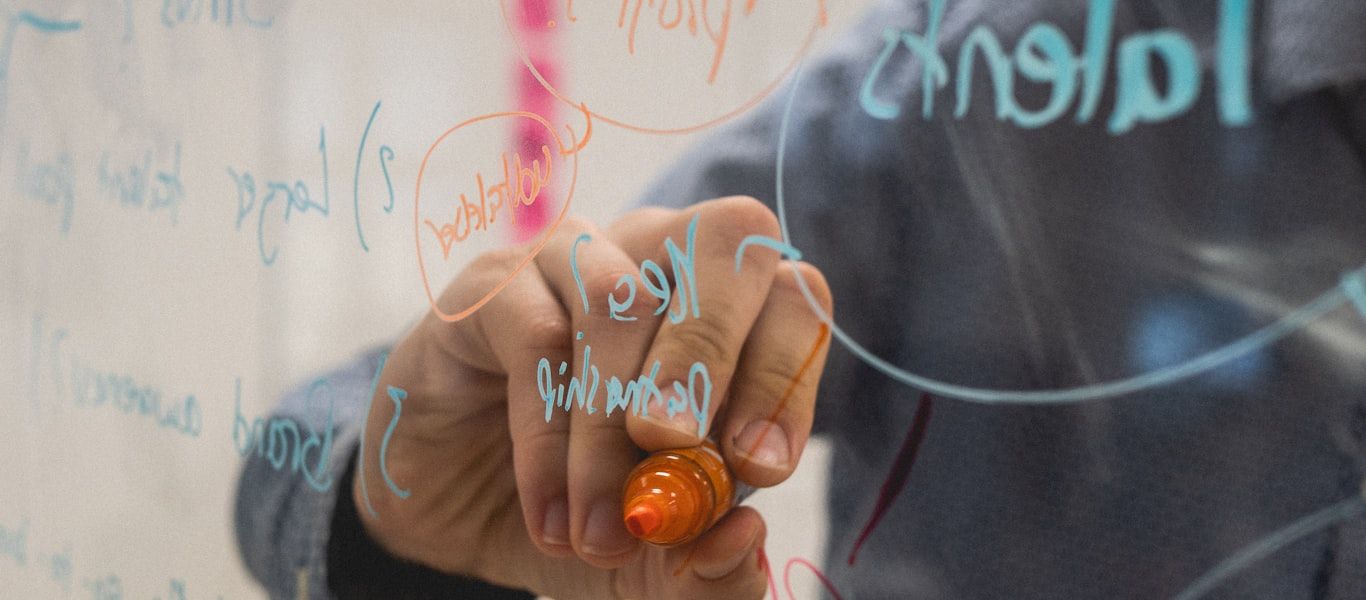A person mapping ideas and connections on a glass board with colored markers