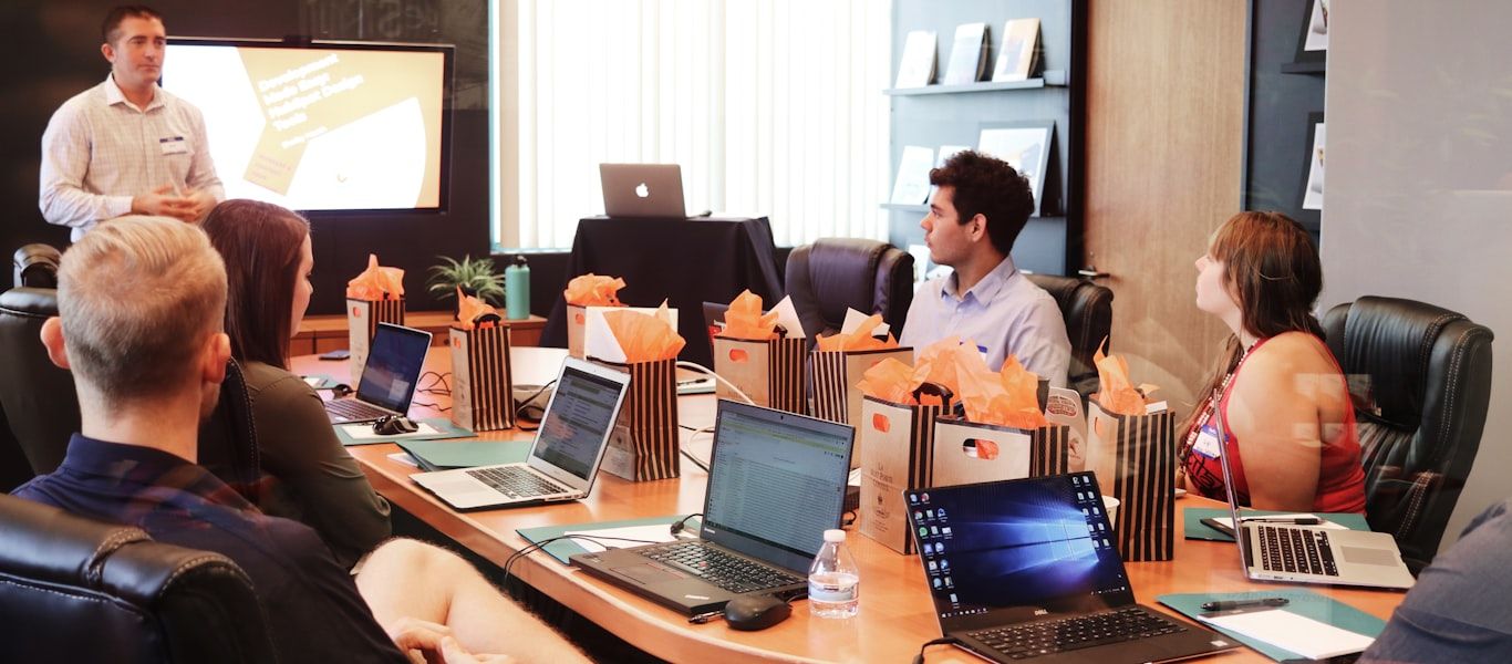 A presenter explaining a concept to colleagues seated with laptops in a meeting room